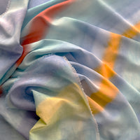 Close-up of a hand-painted Otta silk cotton blend scarf draped softly, showcasing gentle shades of 
blue, yellow, red, orange and green. Lightweight artisan accessory with delicate hand-fringed edges, measuring 70 x 190 cm.
