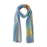 A hand-painted Otta silk cotton blend scarf on a white background, in 
blue, yellow, red, orange and green shades, loosely looped to showcase its full length and delicate texture. Lightweight artisan accessory with hand-fringed edges, measuring 70 x 190 cm.
