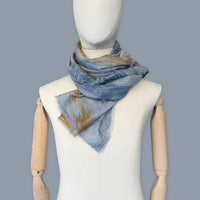 Mannequin wearing scarf on a blue background. Hand-painted silk cotton scarf by Otta-Italy, measuring 67 x 193 cm, featuring 
blue, gray and orange shades. Luxury Italian pure silk cotton blend accessory, soft, fresh and lightweight scarf for women and men.
