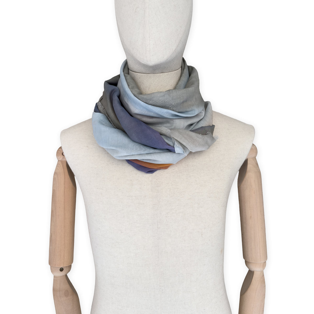 Mannequin wearing a hand-painted Otta silk cotton blend scarf on a white background in 
gray, purple and orange tones. soft, fresh and lightweight, and elegant accessory measuring 70 x 190 cm. Unique artisan scarf with hand-fringed edges, perfect for women and men.
