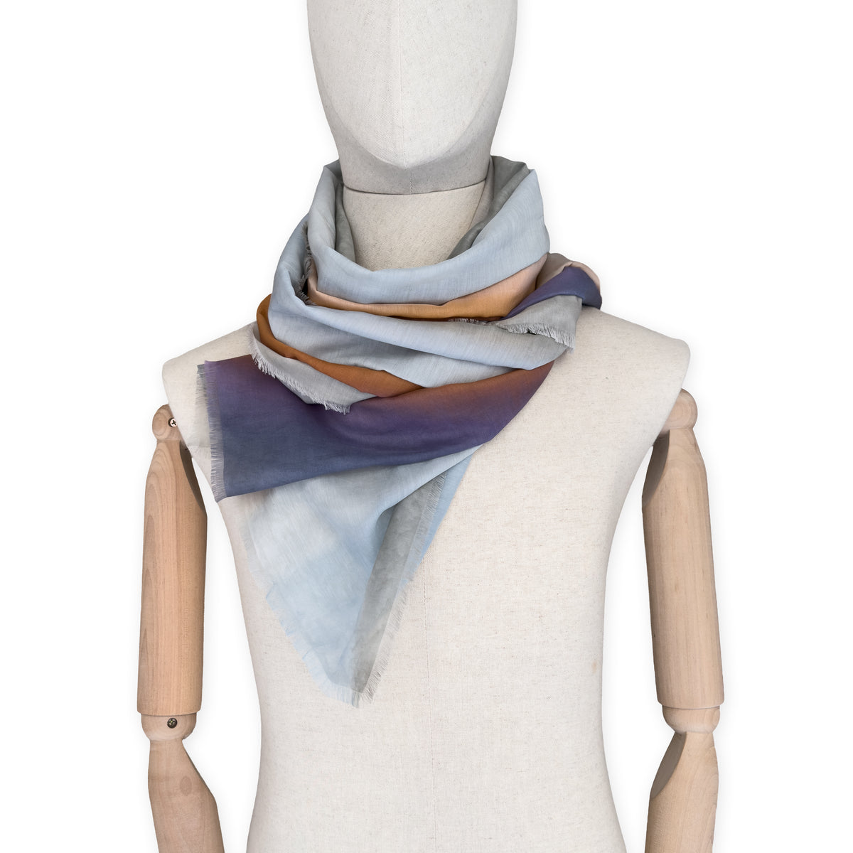 Mannequin wearing a hand-painted Otta silk cotton blend scarf on a white background in 
gray, purple and orange tones. soft, fresh and lightweight, and elegant accessory measuring 70 x 190 cm. Unique artisan scarf with hand-fringed edges, perfect for women and men.
