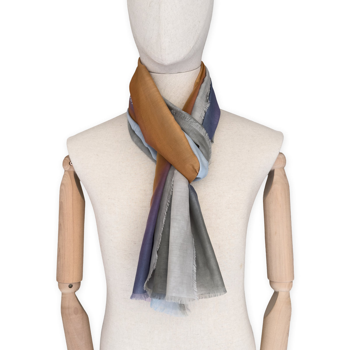 Mannequin wearing a hand-painted Otta silk cotton blend scarf on a white background in 
gray, purple and orange tones. soft, fresh and lightweight, and elegant accessory measuring 70 x 190 cm. Unique artisan scarf with hand-fringed edges, perfect for women and men.
