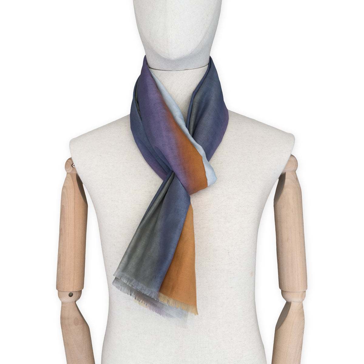 Mannequin wearing a hand-painted Otta silk cotton blend scarf on a white background in 
gray, purple and orange tones. soft, fresh and lightweight, and elegant accessory measuring 70 x 190 cm. Unique artisan scarf with hand-fringed edges, perfect for women and men.

