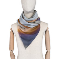 Mannequin wearing a hand-painted Otta silk cotton blend scarf on a white background in 
gray, purple and orange tones. soft, fresh and lightweight, and elegant accessory measuring 70 x 190 cm. Unique artisan scarf with hand-fringed edges, perfect for women and men.
