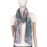 Mannequin wearing a hand-painted Otta silk cotton blend scarf on a white background in 
pink and green e tones. soft, fresh and lightweight, and elegant accessory measuring 70 x 190 cm. Unique artisan scarf with hand-fringed edges, perfect for women and men.
