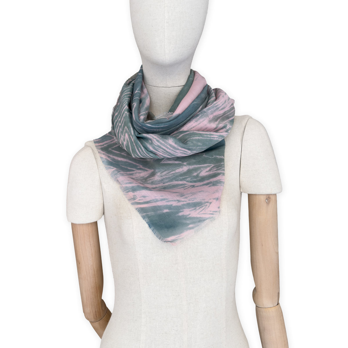 Mannequin wearing a hand-painted Otta silk cotton blend scarf on a white background in 
pink and green e tones. soft, fresh and lightweight, and elegant accessory measuring 70 x 190 cm. Unique artisan scarf with hand-fringed edges, perfect for women and men.
