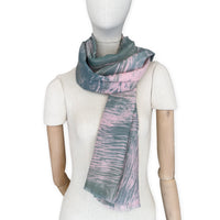 Mannequin wearing a hand-painted Otta silk cotton blend scarf on a white background in 
pink and green e tones. soft, fresh and lightweight, and elegant accessory measuring 70 x 190 cm. Unique artisan scarf with hand-fringed edges, perfect for women and men.
