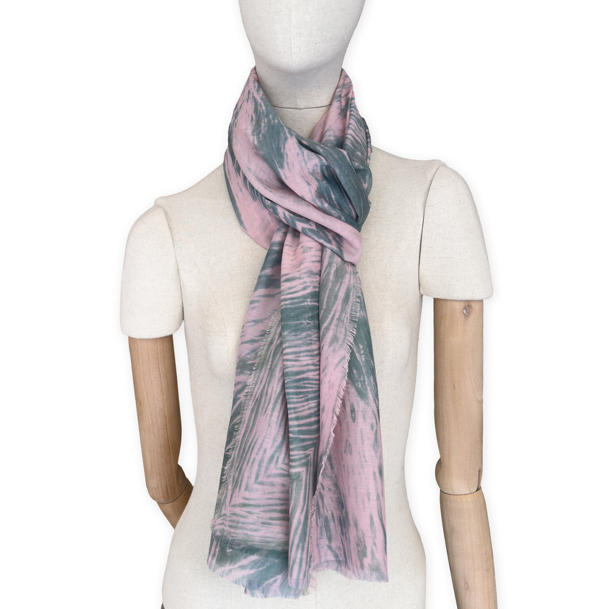 Mannequin wearing a hand-painted Otta silk cotton blend scarf on a white background in 
pink and green e tones. soft, fresh and lightweight, and elegant accessory measuring 70 x 190 cm. Unique artisan scarf with hand-fringed edges, perfect for women and men.
