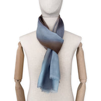 Mannequin wearing an elegant hand-painted Otta pure cashmere scarf on a white background. Warm blue, beige, orange, gray and brown tones.
