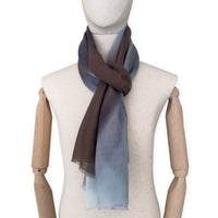 Mannequin wearing an elegant hand-painted Otta pure cashmere scarf on a white background. Warm blue, beige, orange, gray and brown tones.
