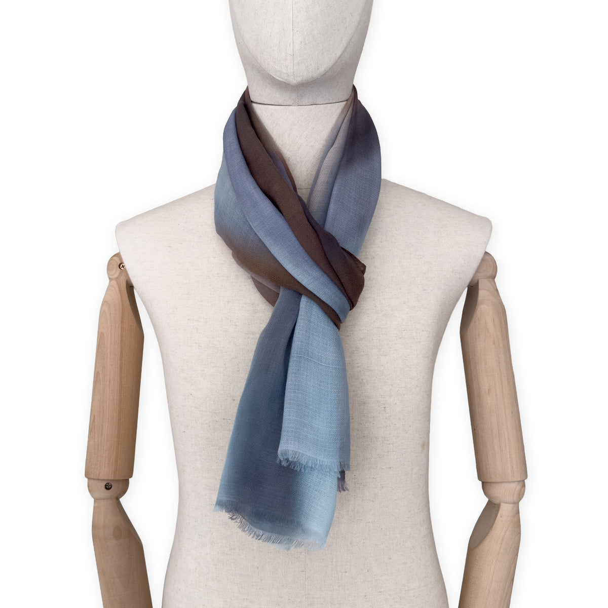 Mannequin wearing an elegant hand-painted Otta pure cashmere scarf on a white background. Warm blue, beige, orange, gray and brown tones.
