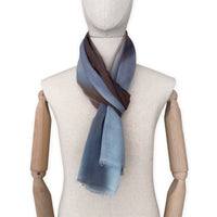 Mannequin wearing an elegant hand-painted Otta pure cashmere scarf on a white background. Warm blue, beige, orange, gray and brown tones.
