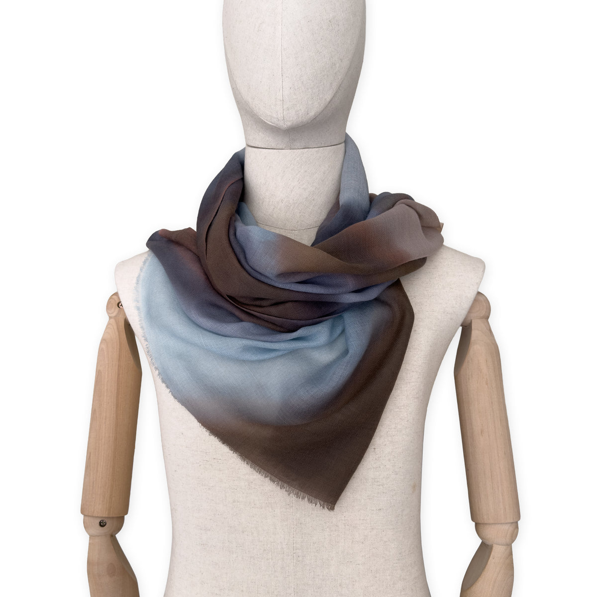Mannequin wearing an elegant hand-painted Otta pure cashmere scarf on a white background. Warm blue, beige, orange, gray and brown tones.

