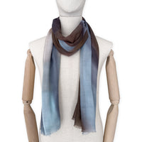Mannequin wearing an elegant hand-painted Otta pure cashmere scarf on a white background. Warm blue, beige, orange, gray and brown tones.
