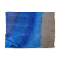 Folded fabric with blue and brown gradient on a white background. cashmere-scarf-hand-painted-69x207cm-indigo-sky-blue-midnight-blue-brown-otta-italy