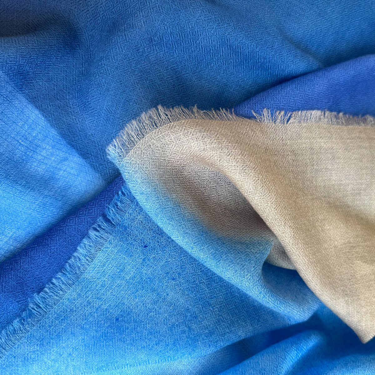 Close-up of blue and beige fabric with frayed edges. cashmere-scarf-hand-painted-69x207cm-indigo-sky-blue-midnight-blue-brown-otta-italy
