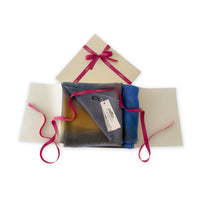 Luxury gift box with a pink ribbon containing a hand-painted Otta pure cashmere scarf on a white background.
