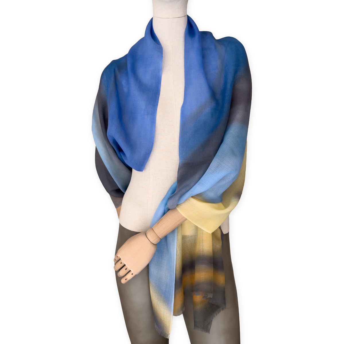 Mannequin wearing an elegant hand-painted Otta pure cashmere scarf on a white background. Warm blue, yellow, orange, gray and brown tones.
