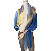 Mannequin wearing an elegant hand-painted Otta pure cashmere scarf on a white background. Warm blue, yellow, orange, gray and brown tones.
