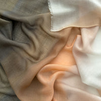 Close-up of hand-painted Otta pure cashmere scarf showcasing soft brown, peach, beige and gray shades with delicate hand-fringed edges.
