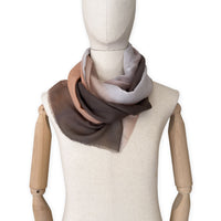 Mannequin wearing an elegant hand-painted Otta pure cashmere scarf on a white background. Warm brown, peach, beige and gray tones.
