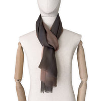 Mannequin wearing an elegant hand-painted Otta pure cashmere scarf on a white background. Warm brown, peach, beige and gray tones.
