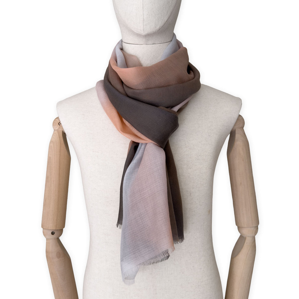 Mannequin wearing an elegant hand-painted Otta pure cashmere scarf on a white background. Warm brown, peach, beige and gray tones.
