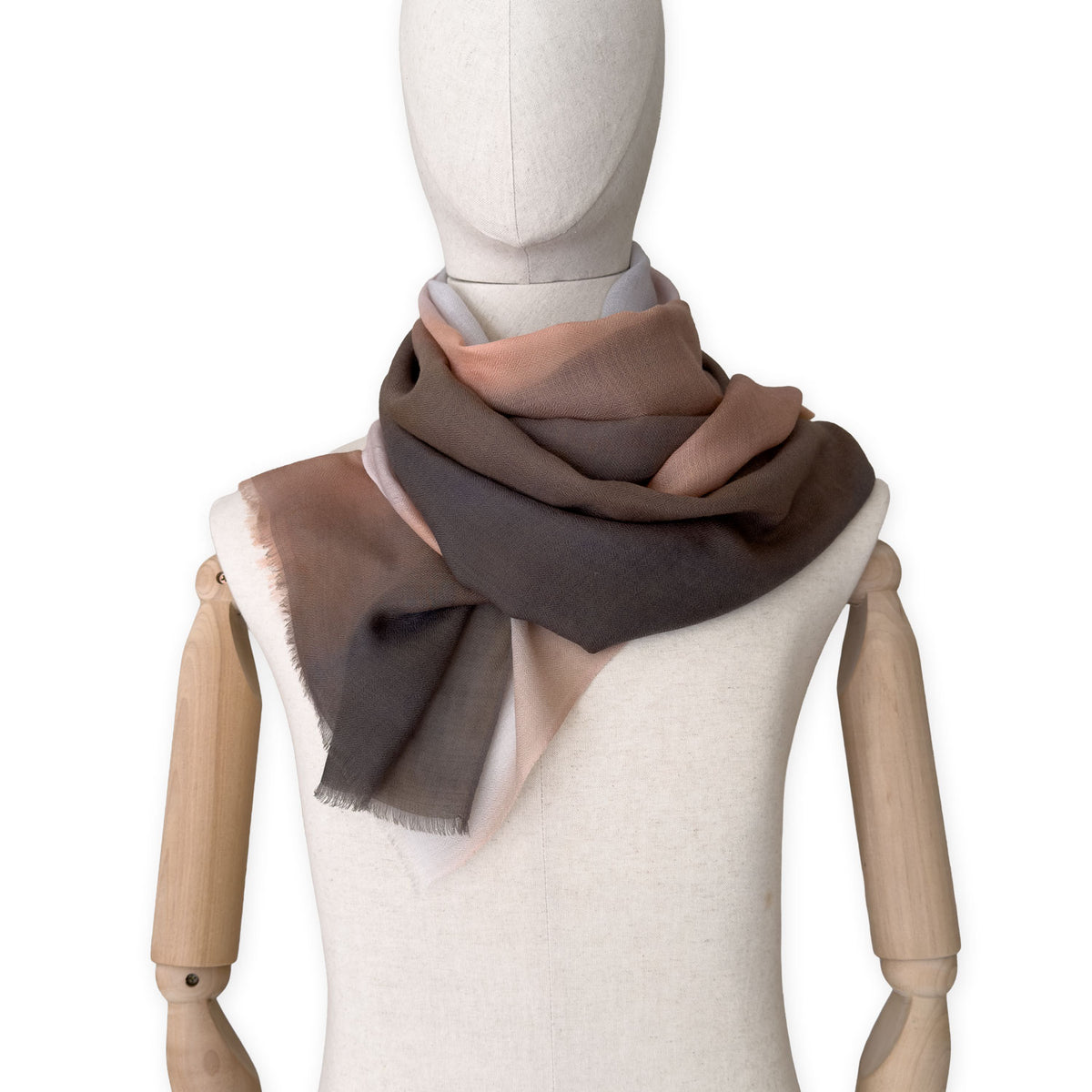 Mannequin wearing an elegant hand-painted Otta pure cashmere scarf on a white background. Warm brown, peach, beige and gray tones.
