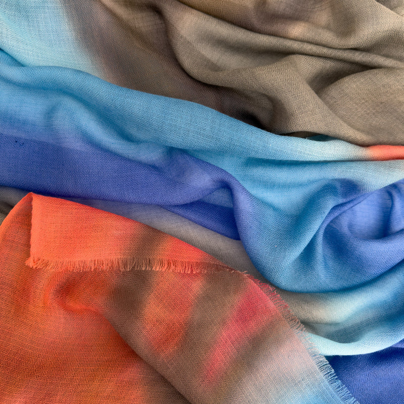 Close-up of hand-painted Otta pure cashmere scarf showcasing soft brown, blue, coral and gray shades with delicate hand-fringed edges.
