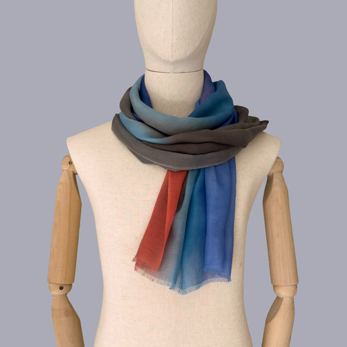 Mannequin wearing a hand-painted pure cashmere scarf by Otta-Italy, gray background. Brown, blue, coral and gray shades. 69 x 202 cm.
