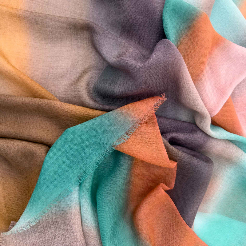 Close-up of hand-painted Otta pure cashmere scarf showcasing soft brown, emerald green, coral and gray shades with delicate hand-fringed edges.
