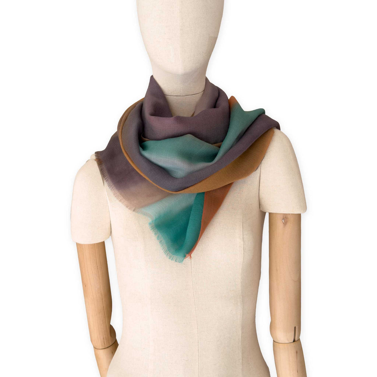 Mannequin wearing an elegant hand-painted Otta pure cashmere scarf on a white background. Warm brown, emerald green, coral and gray and brown tones.
