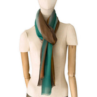 Mannequin wearing an elegant hand-painted Otta pure cashmere scarf on a white background. Warm brown, emerald green, coral and gray and brown tones.
