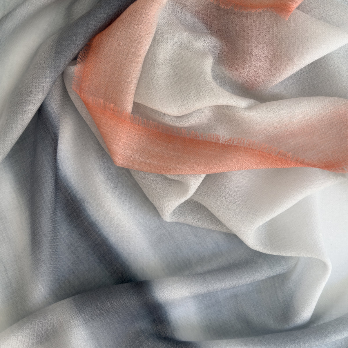 Close-up of soft fabric. Hand-painted pure cashmere scarf by Otta-Italy, 66 x 198 cm, featuring grey and coral. Luxury Italian cashmere accessory, soft and warm scarf for women and men.
