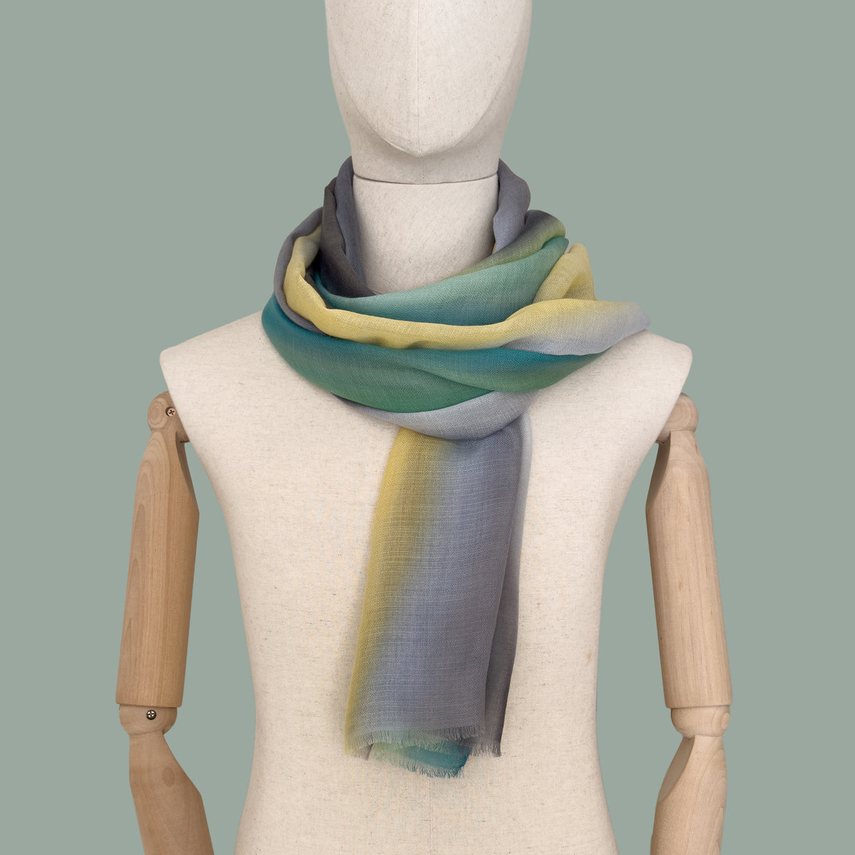 Mannequin wearing scarf on a gray background. Hand-painted cashmere scarf by Otta-Italy, 68 x 202 cm, featuring 
green, yellow, gray and brown. Luxury Italian pure cashmere accessory, soft and warm scarf for women and men.
