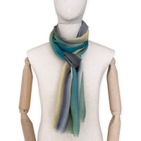 Mannequin wearing a hand-painted Otta cashmere scarf on a white background in 
green, yellow, gray and brown tones. Lightweight, warm, and elegant accessory measuring 68 x 202 cm. Unique artisan scarf with hand-fringed edges, perfect for women and men.
