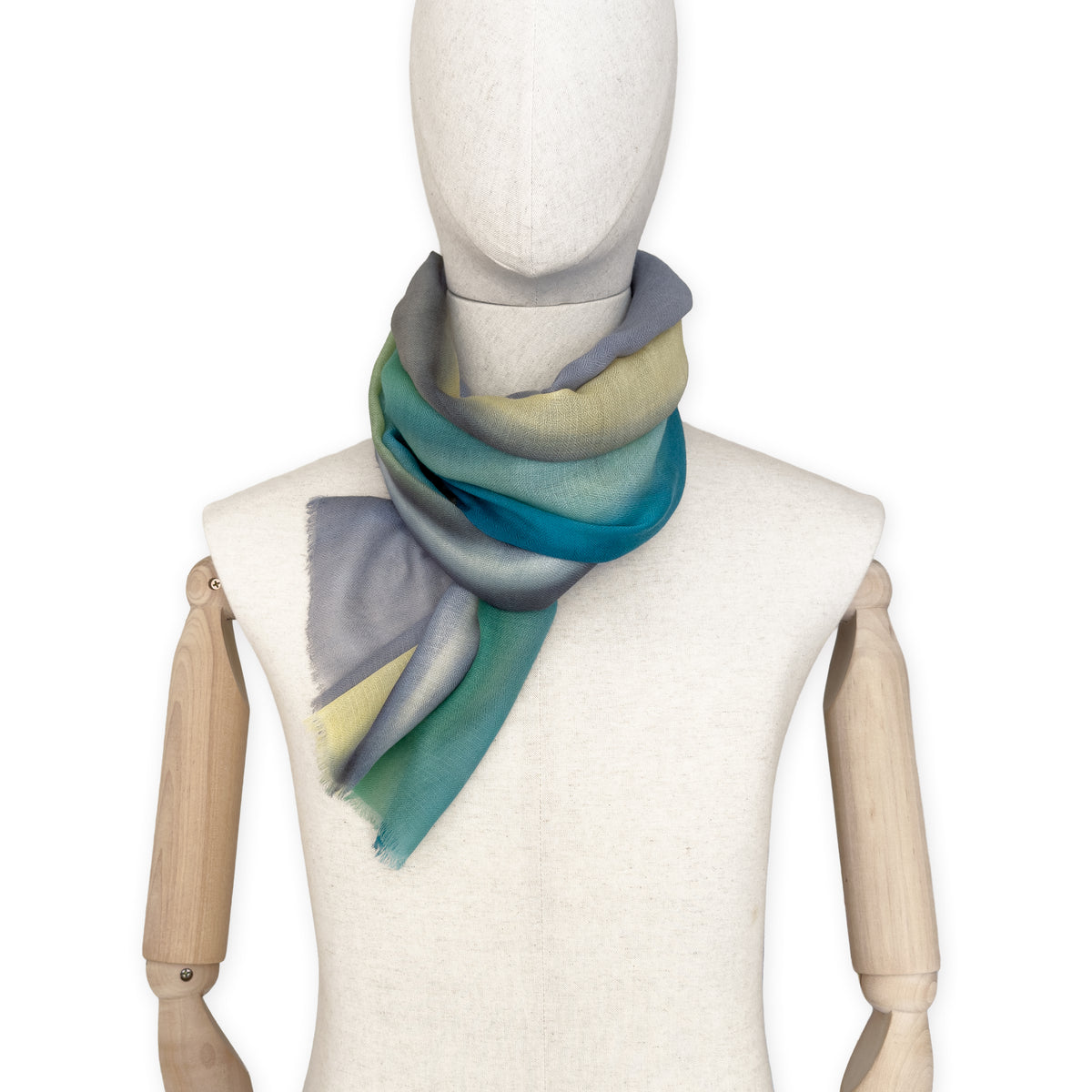 Mannequin wearing a hand-painted Otta cashmere scarf on a white background in 
green, yellow, gray and brown tones. Lightweight, warm, and elegant accessory measuring 68 x 202 cm. Unique artisan scarf with hand-fringed edges, perfect for women and men.
