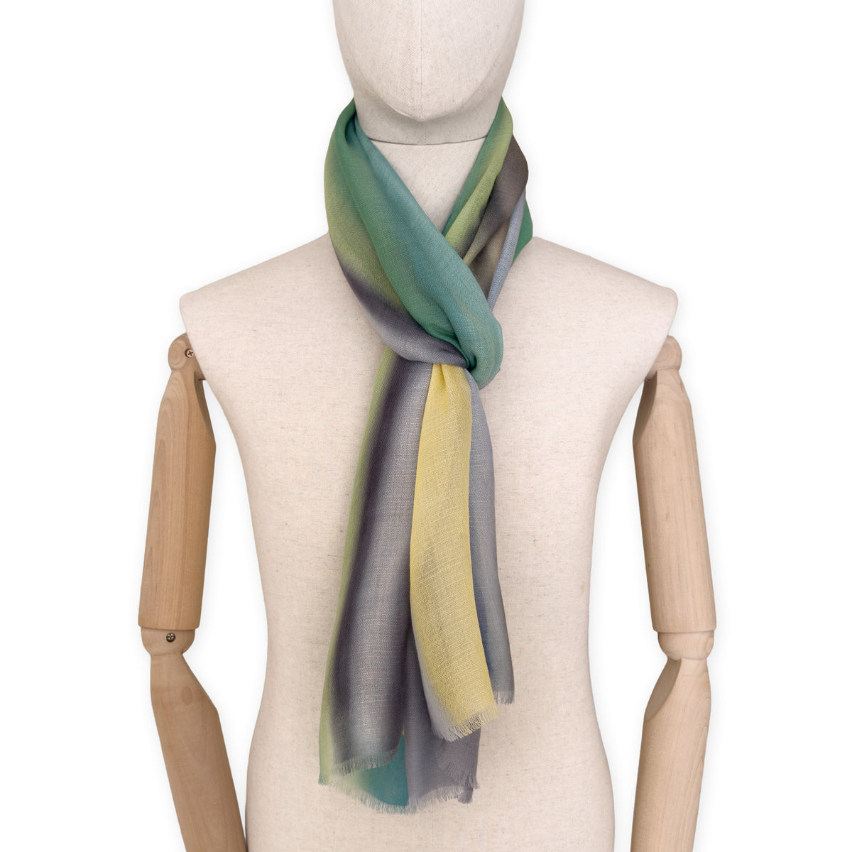 Mannequin wearing a hand-painted Otta cashmere scarf on a white background in 
green, yellow, gray and brown tones. Lightweight, warm, and elegant accessory measuring 68 x 202 cm. Unique artisan scarf with hand-fringed edges, perfect for women and men.
