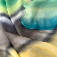 
Close-up of a hand-painted Otta cashmere scarf draped softly, showcasing gentle shades of 
green, yellow, gray and brown. Lightweight artisan accessory with delicate hand-fringed edges, measuring 68 x 202 cm.

