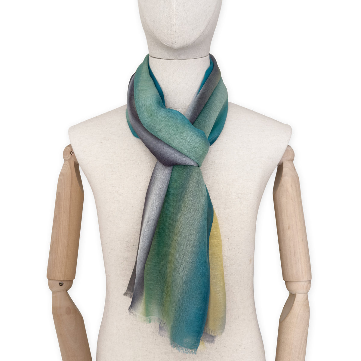 Mannequin wearing a hand-painted Otta cashmere scarf on a white background in 
green, yellow, gray and brown tones. Lightweight, warm, and elegant accessory measuring 68 x 202 cm. Unique artisan scarf with hand-fringed edges, perfect for women and men.
