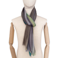 Mannequin wearing a hand-painted Otta cashmere scarf on a white background in 
green, yellow, gray and brown tones. Lightweight, warm, and elegant accessory measuring 68 x 202 cm. Unique artisan scarf with hand-fringed edges, perfect for women and men.
