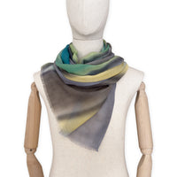 Mannequin wearing a hand-painted Otta cashmere scarf on a white background in 
green, yellow, gray and brown tones. Lightweight, warm, and elegant accessory measuring 68 x 202 cm. Unique artisan scarf with hand-fringed edges, perfect for women and men.
