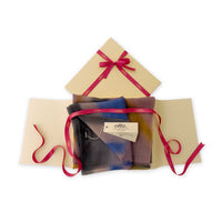 Luxury gift box with a pink ribbon containing a hand-painted Otta pure cashmere scarf on a white background.

