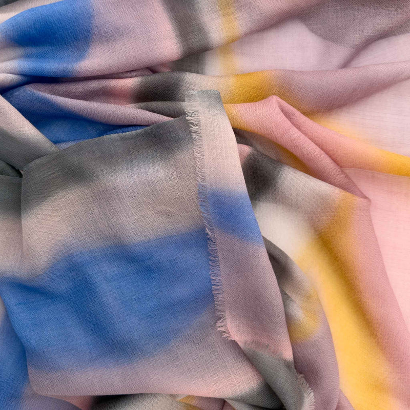 Close-up of hand-painted Otta pure cashmere scarf showcasing soft pink, orange, blue and gray shades with delicate hand-fringed edges.
