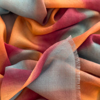 Close-up of a hand-painted Otta cashmere scarf draped softly, showcasing gentle shades of 
orange, red and blue. Lightweight artisan accessory with delicate hand-fringed edges, measuring 69 x 201 cm.
