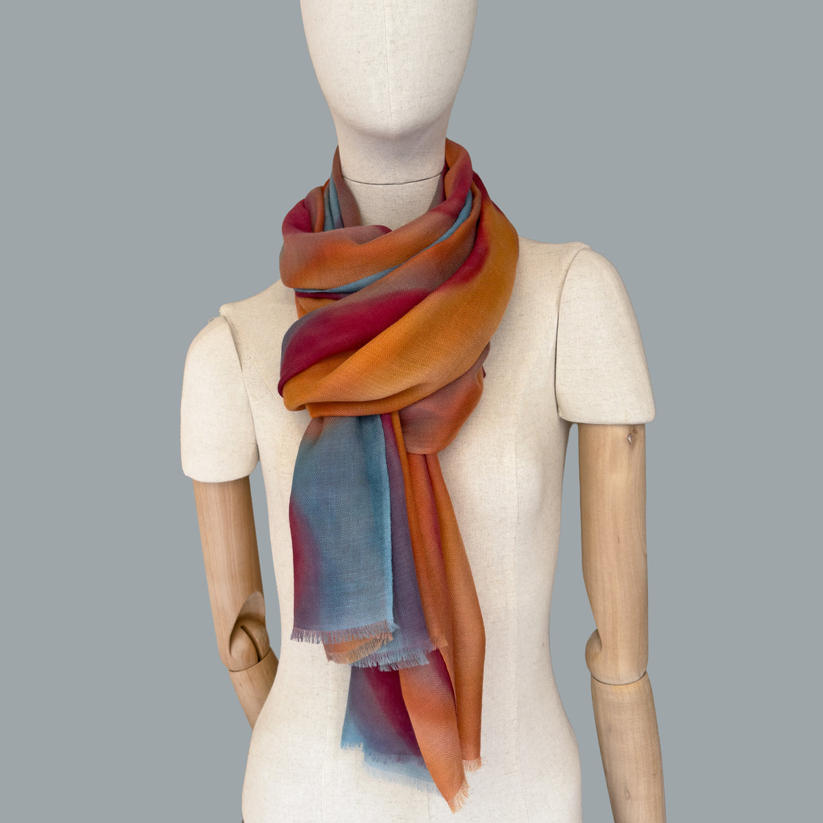 Mannequin wearing scarf on a gray background. Hand-painted cashmere scarf by Otta-Italy, 69 x 201 cm, featuring 
orange, red and blue. Luxury Italian pure cashmere accessory, soft and warm scarf for women and men.
