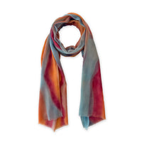  Hand-painted Otta cashmere scarf in 
orange, red and blue, loosely looped to showcase its full length and delicate texture in white background. Lightweight artisan accessory with hand-fringed edges, measuring 69 x 201 cm.

