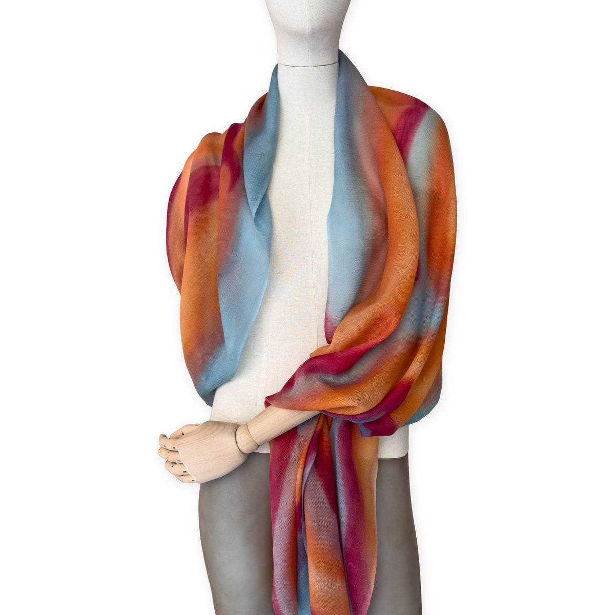 Mannequin wearing a hand-painted Otta cashmere scarf on a white background in 
orange, red and blue tones. Lightweight, warm, and elegant accessory measuring 69 x 201 cm. Unique artisan scarf with hand-fringed edges, perfect for women and men.

