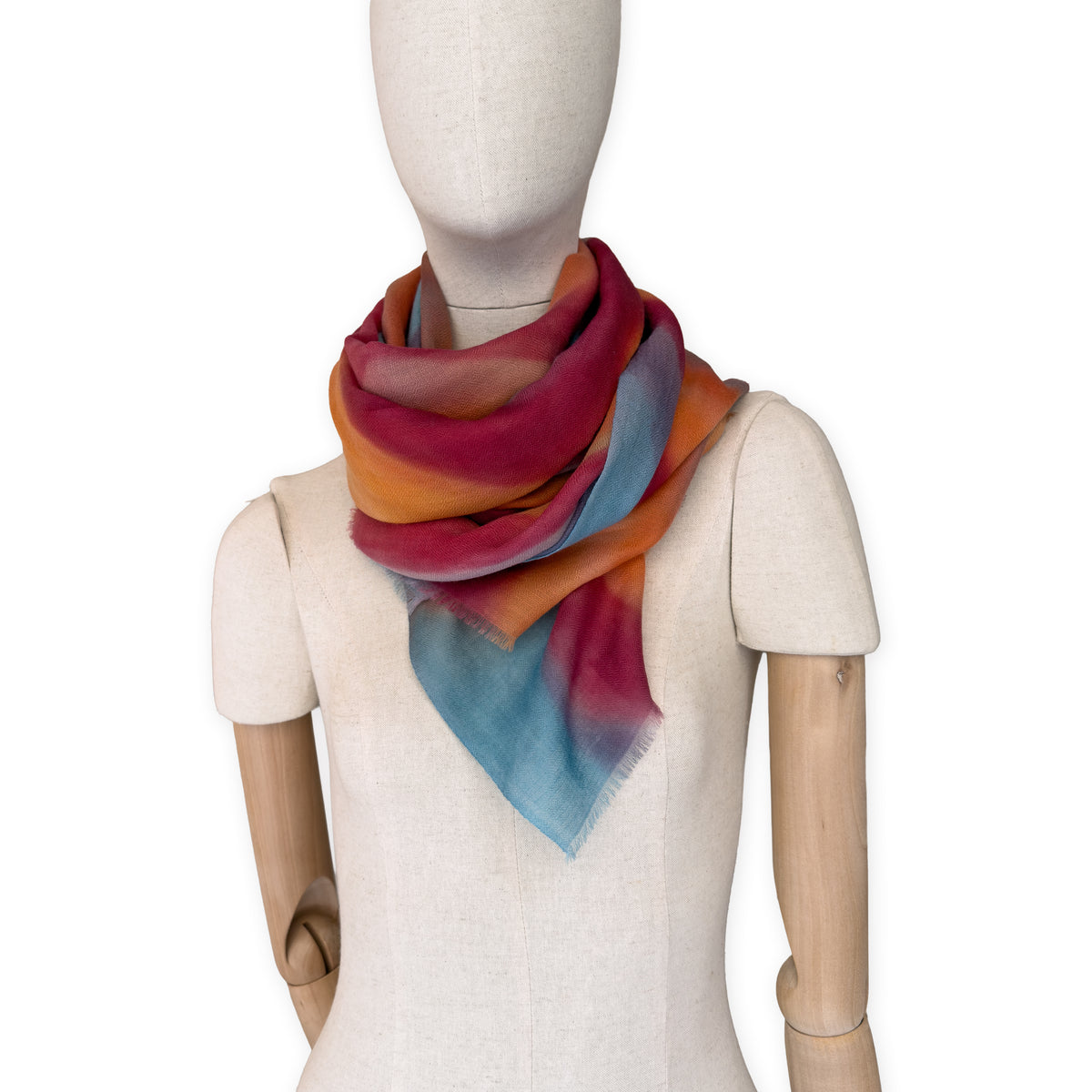 Mannequin wearing a hand-painted Otta cashmere scarf on a white background in 
orange, red and blue tones. Lightweight, warm, and elegant accessory measuring 69 x 201 cm. Unique artisan scarf with hand-fringed edges, perfect for women and men.
