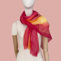 Mannequin wearing a hand-painted pure cashmere scarf by Otta-Italy, pink background. Red, orange and yellow shades. 69 x 200 cm.
